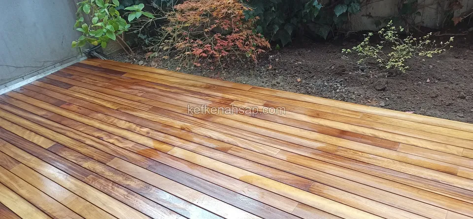 Glossy varnished orange-brown deck boards stretching along a wall and shrubbery