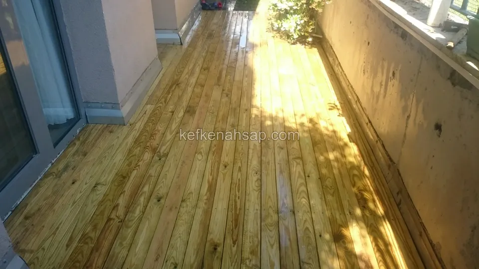 Timber deck running between a wall and a glass door, with sun and shade mixing across the boards