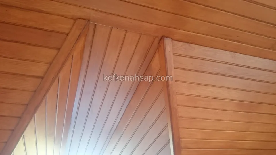 Eğimli tavanda bal rengi vernikli ahşap lambri kaplama, köşelerde kalın ahşap kirişler ve farklı yönlerde uzanan tahtalar