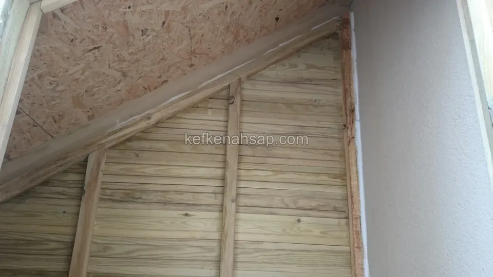 Eğimli tavanın üstünde OSB levha, alt kısımda çıtalara çakılmış açık renkli tahta kaplama