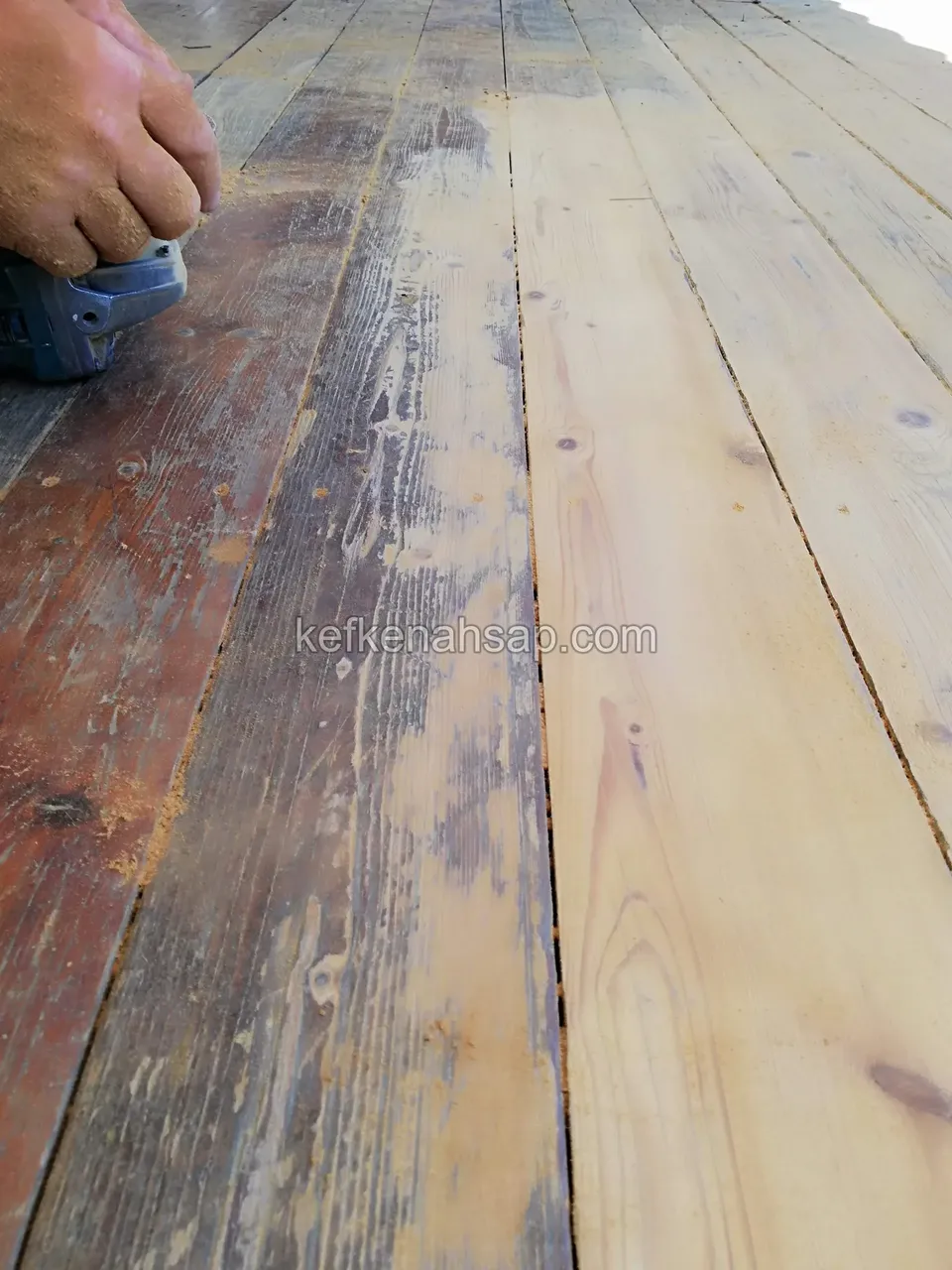 Alte gestrichene Terrassendielen werden mit einem Handschleifer geschliffen, auf der Oberfläche sind Farbreste