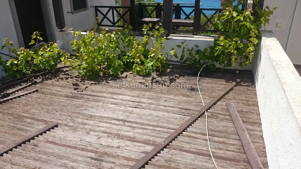 Old greyed deck on a balcony, with removed pieces of board lying on it and vine leaves and a cable at the edge