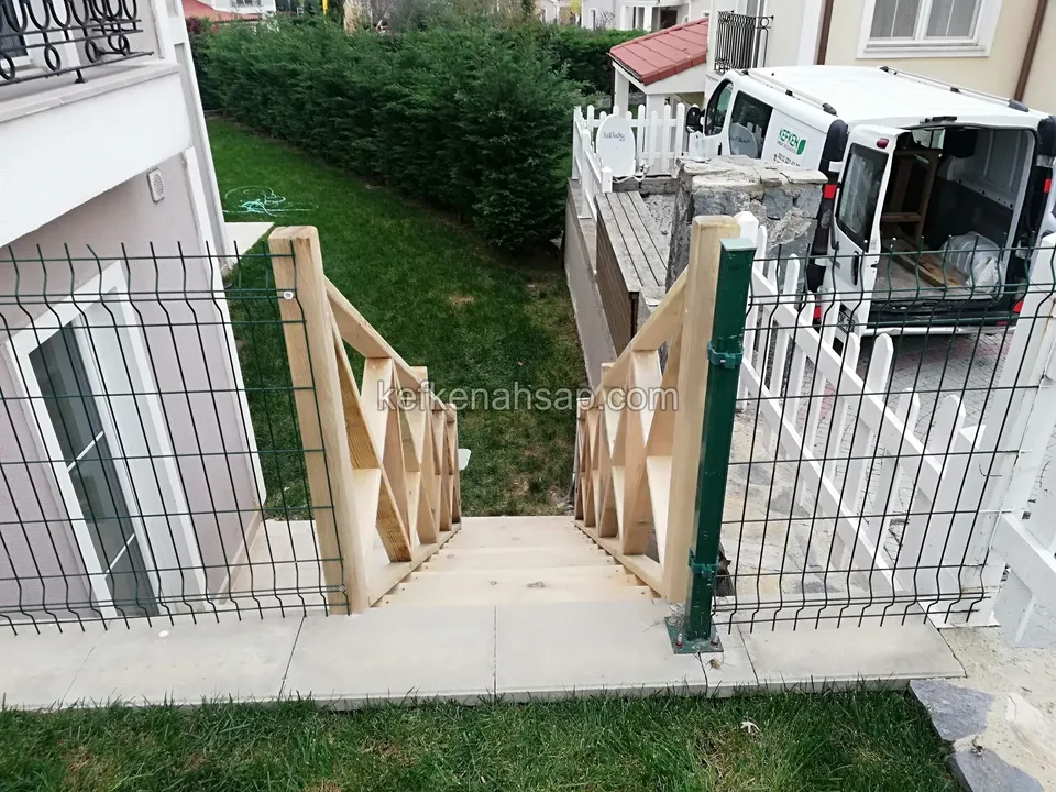 Holztreppe mit Kreuzstreben-Geländer im Gang zwischen zwei Gebäuden, seitlich Maschenzaun, dahinter ein weißes Fahrzeug