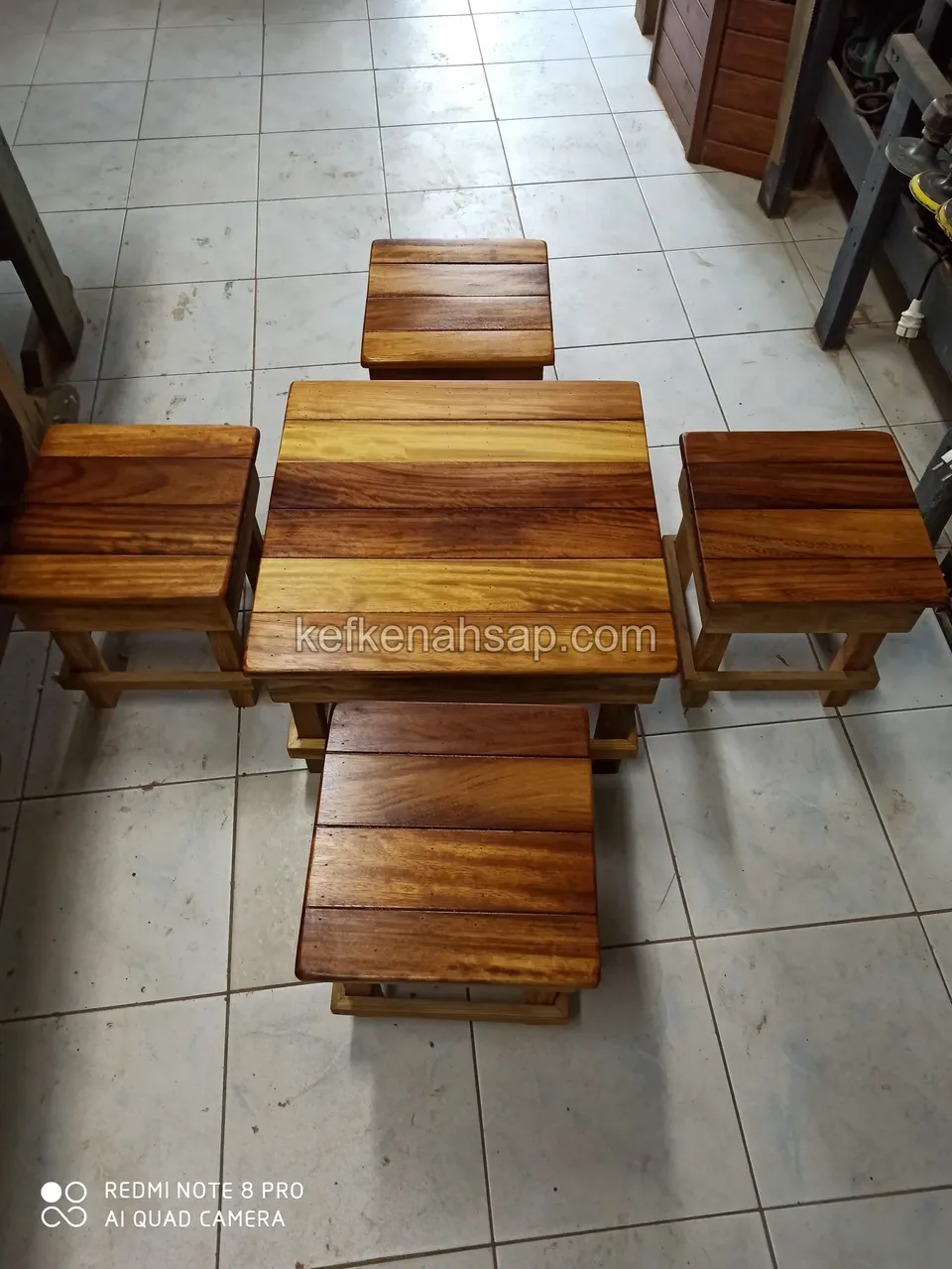 From above, four small timber stools set around a small low table in the middle on a tiled floor, all glossy-varnished