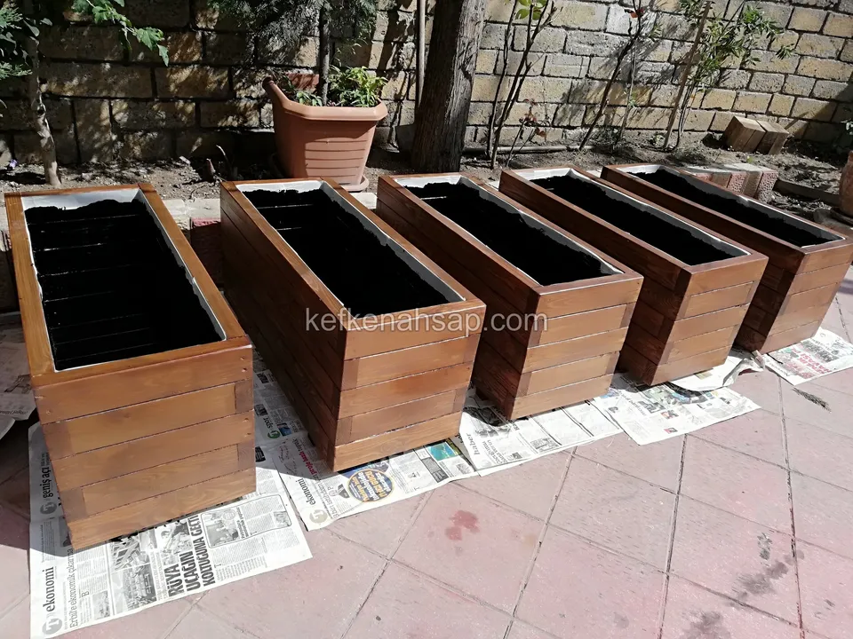 Gazetelerin üzerine yan yana dizilmiş, içleri siyah astarlı ahşap çiçekliklerin biraz yüksekten görünümü