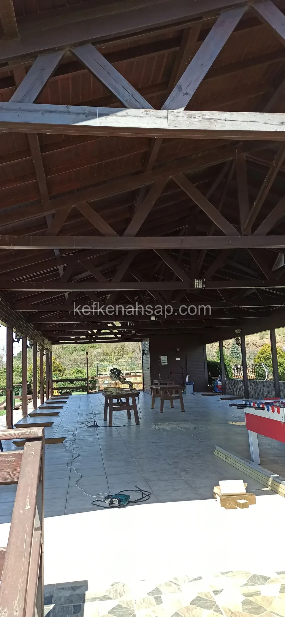 Geniş ahşap çatı makaslarının altında uzayan açık salon, boş döşeme, uzakta masalar