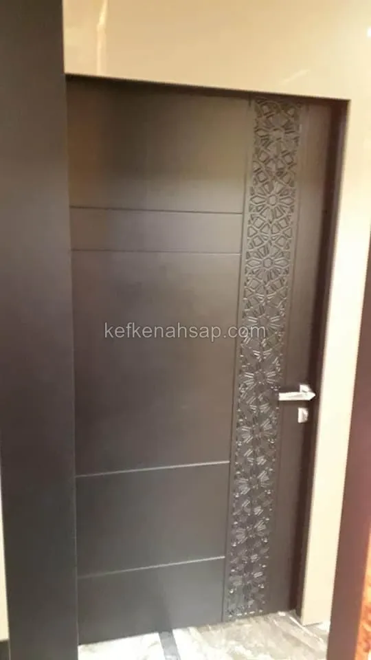 باب خشبي مطلي بالبني الداكن بلوح بخياطة أفقية وبجانبه شريط منحوت بنقش هندسي ومقبض معدني