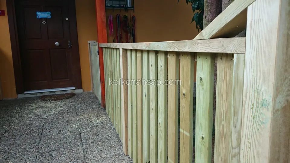 Bina girişinin önünde, kalın küpeşteli dikey tahtalı ahşap korkuluk ve yanında küçük bir ahşap kapı