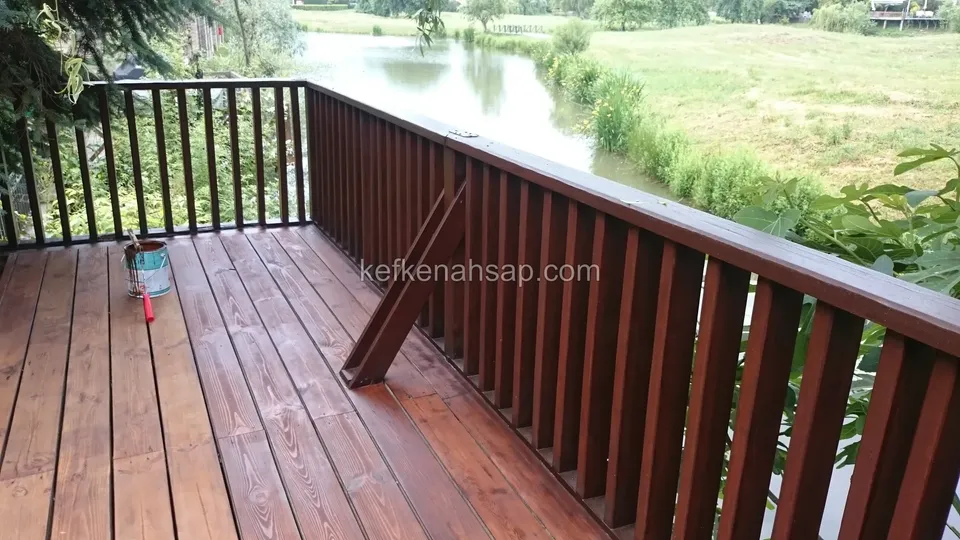 Deck painted dark reddish-brown on a balcony facing a lake with a dark railing, with a paint tin in the corner