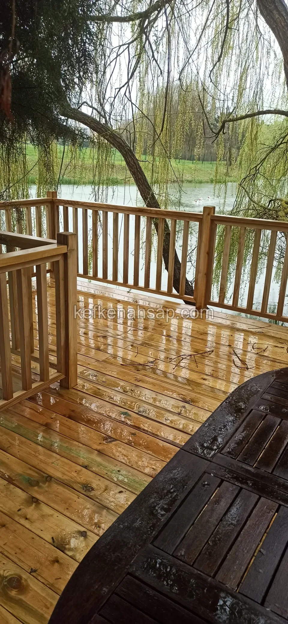 Deck mit Seeblick, Holzgeländer und einem dunklen Holztisch in der Ecke
