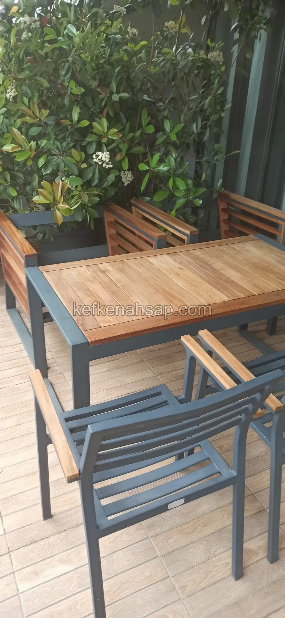 Terrace set of a timber-top table and grey metal chairs in front of plants