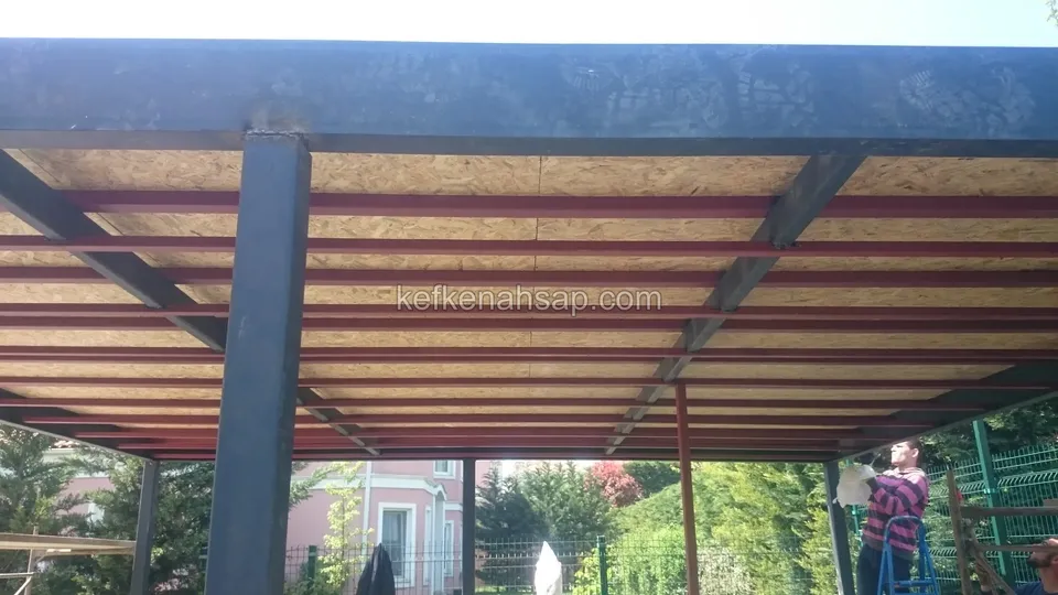 Gri metal çerçeveli pergolanın altından kırmızı boyalı profiller ve üstüne serilmiş OSB levhalar görünüyor