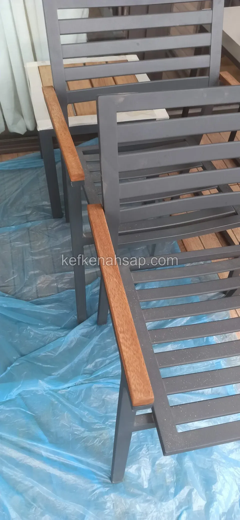 Mavi örtünün üstünde duran koyu gri metal sandalyeler ve ahşap kolçakları