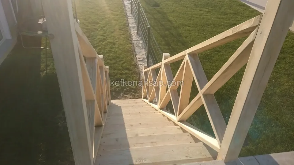 Gün batımı ışığında üstten görünen basamaklar ve çaprazlı korkuluk; iki yanda çimlik