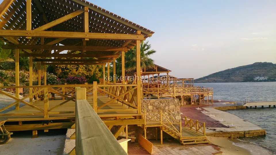 Kıyıda çapraz korkuluklu deck'ler, çıtalı çatılı kamelya ve kumsala inen ahşap merdivenler