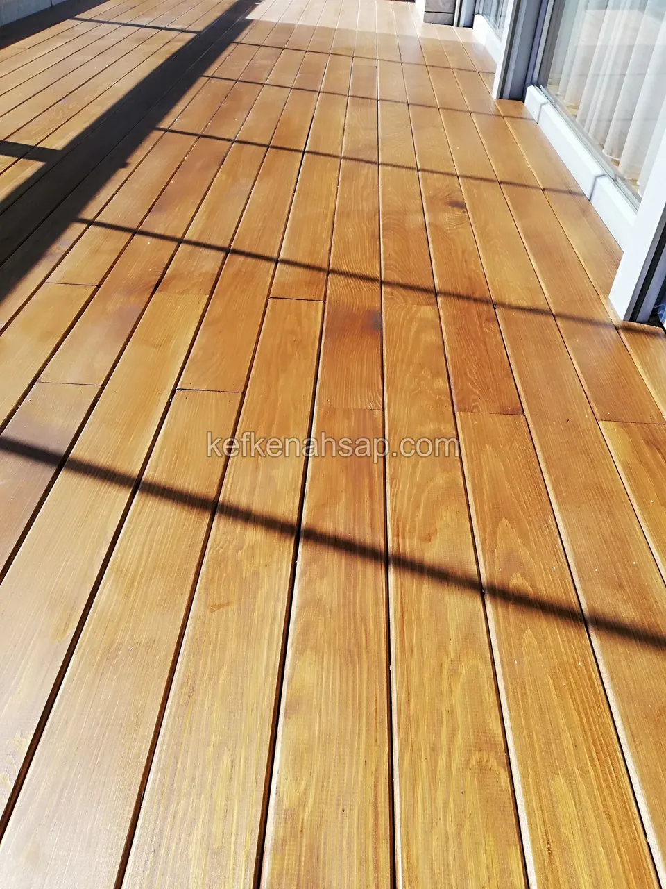 Orange-yellow deck boards on a sunlit balcony with shadows of the glazing falling across them