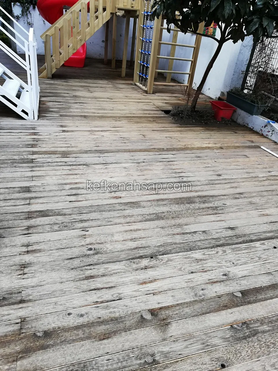 Altes verwittertes, ergrautes und abgenutztes Holzdeck, dahinter ein Holzspielgerüst mit Treppe