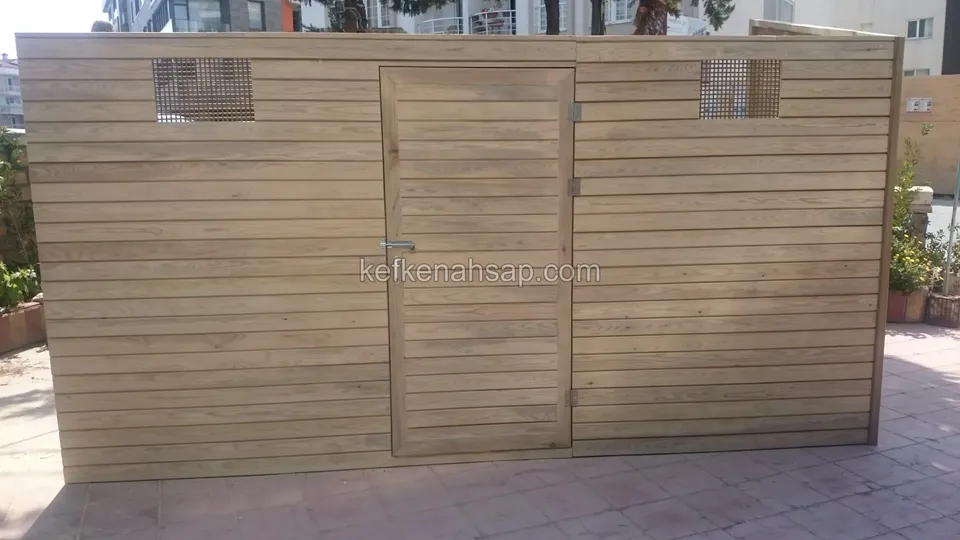 Karo zemin üzerinde yatay tahtalı, ortada kapısı ve üstte iki kafes havalandırması olan ahşap depo