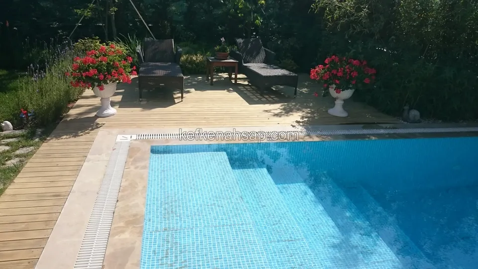 The steps of a mosaic-tiled pool and the deck strip beside them, with red flowers in white planters on both sides