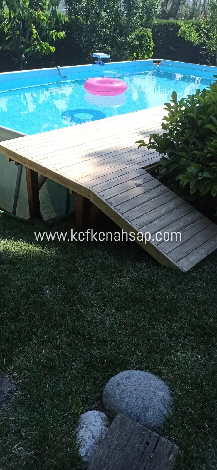Holzdeckplattform am Aufstellpool im Rasengarten mit geneigter Holzrampe zum Boden, im Pool ein rosa Schwimmtier