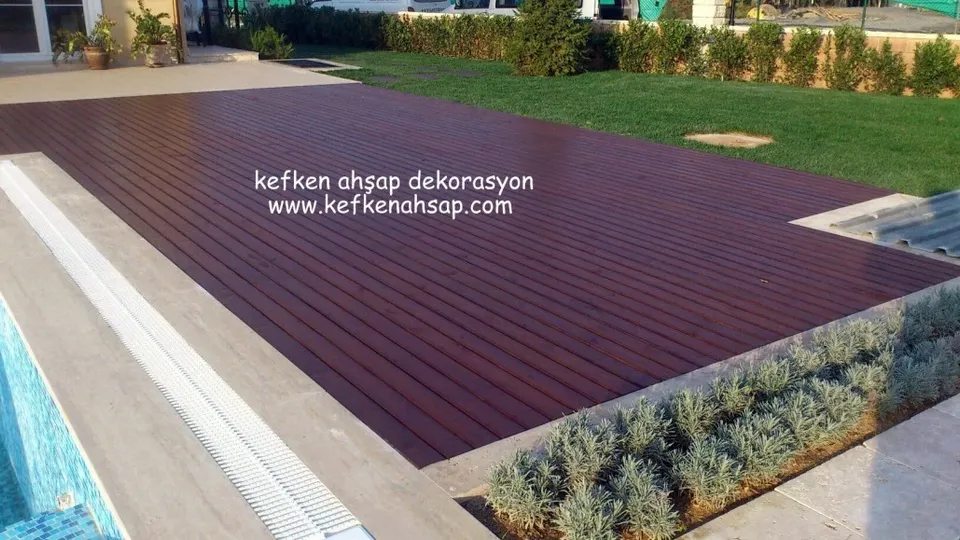 Havuz kenarında çimenlik bahçeye uzanan, koyu kızıl kahverengi geniş ahşap deck zemin; yanında lavanta ve taş kaplama