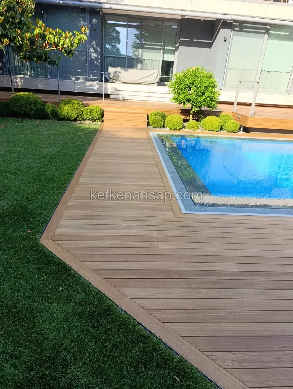 Light brown wood deck laid diagonally between a lawn and a pool, with a stepped terrace behind