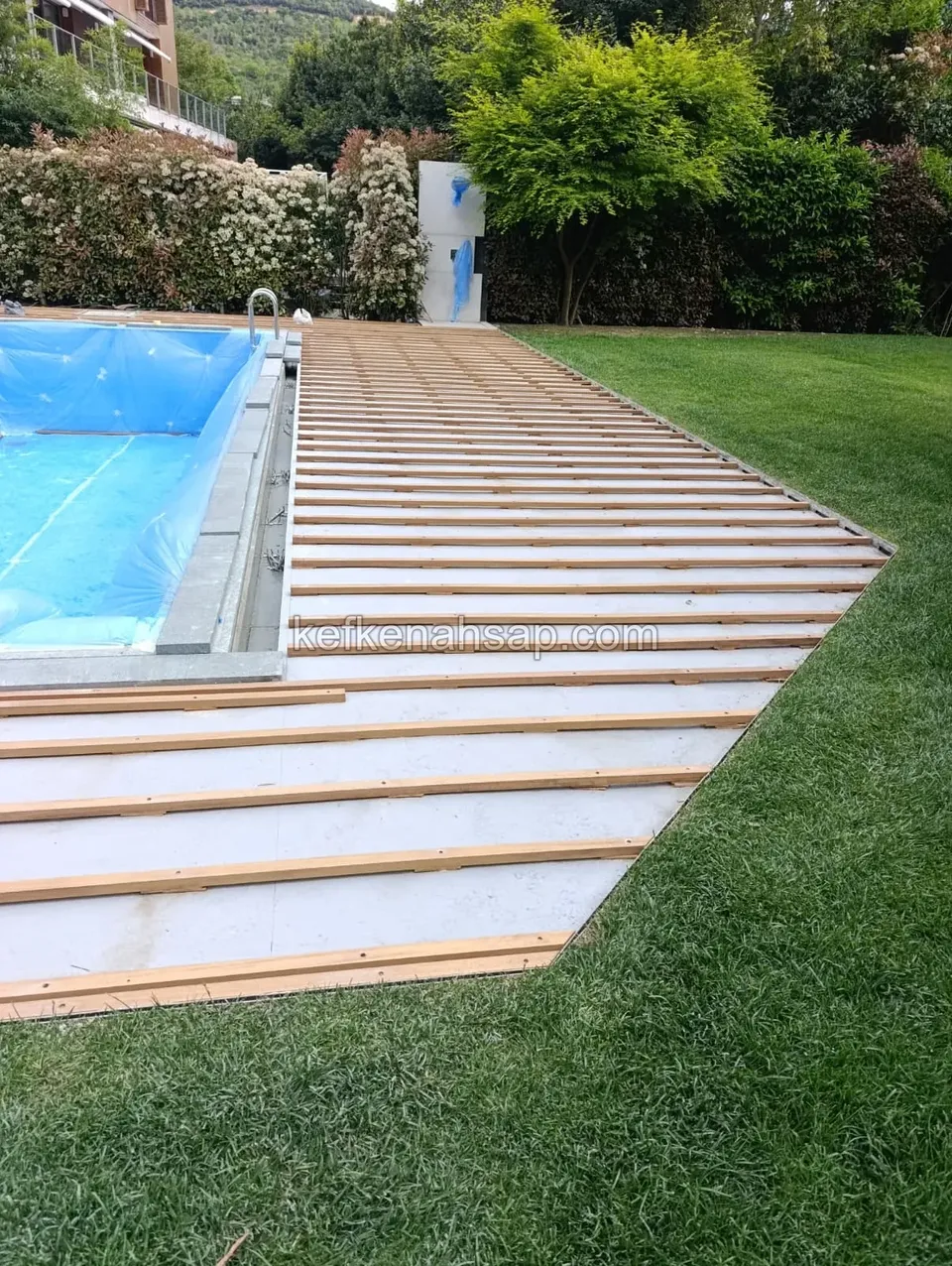 Wooden joists laid across a base beside a garden pool and lawn, with the deck boards not yet installed