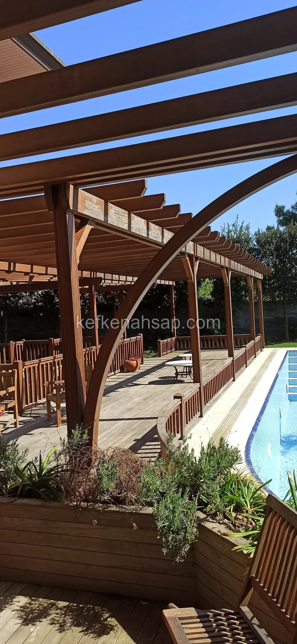 Havuz kenarında kemer biçiminde bükülmüş pergola kirişleri, ahşap deck, bitkili ahşap saksılık ve bank