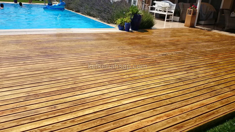 Havuz önünde yayılan bal rengi geniş deck; arkada beyaz bir bahçe bankı, lavantalar ve saksılar