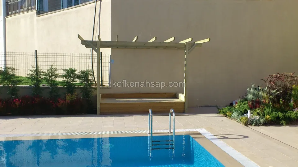 Havuzun yanında sıvalı duvar önünde pergola, altında ahşap oturma bankı ve ön tarafta merdivenli havuz