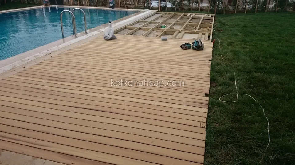 Havuz kenarında uzanan deck yüzeyi, uçta çıplak taşıyıcı çerçeve ve yerde matkap ile el aletleri