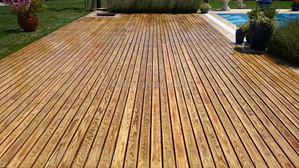 Havuza doğru uzanan, altın sarısı tonlarda ve cilalı parlak deck; kenarda koyu mavi saksılar ve bitkiler