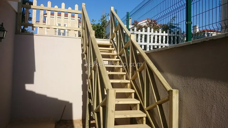 İki sıvalı duvarın arasında, beyaz ahşap çite doğru yükselen çapraz korkuluklu ahşap merdiven