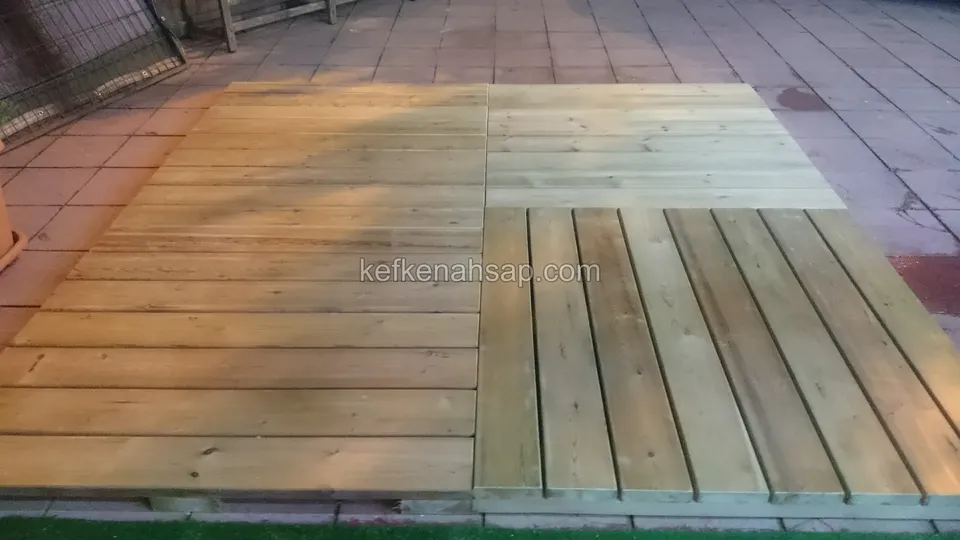 Parke taşlı zeminde birleştirilmiş açık yeşilimsi emprenyeli deck panelleri, sağ altta tahtaları dik yöne dönen panel