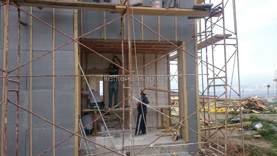 Mit Holzlatten über Dämmplatten vorbereitete Fassadenunterkonstruktion an einem eingerüsteten Gebäude, Arbeiter am Werk