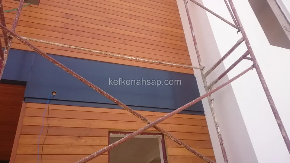 İskeleli binada yatay ahşap cephe kaplaması, ortada koyu membran bant ve altında pencere boşluğu