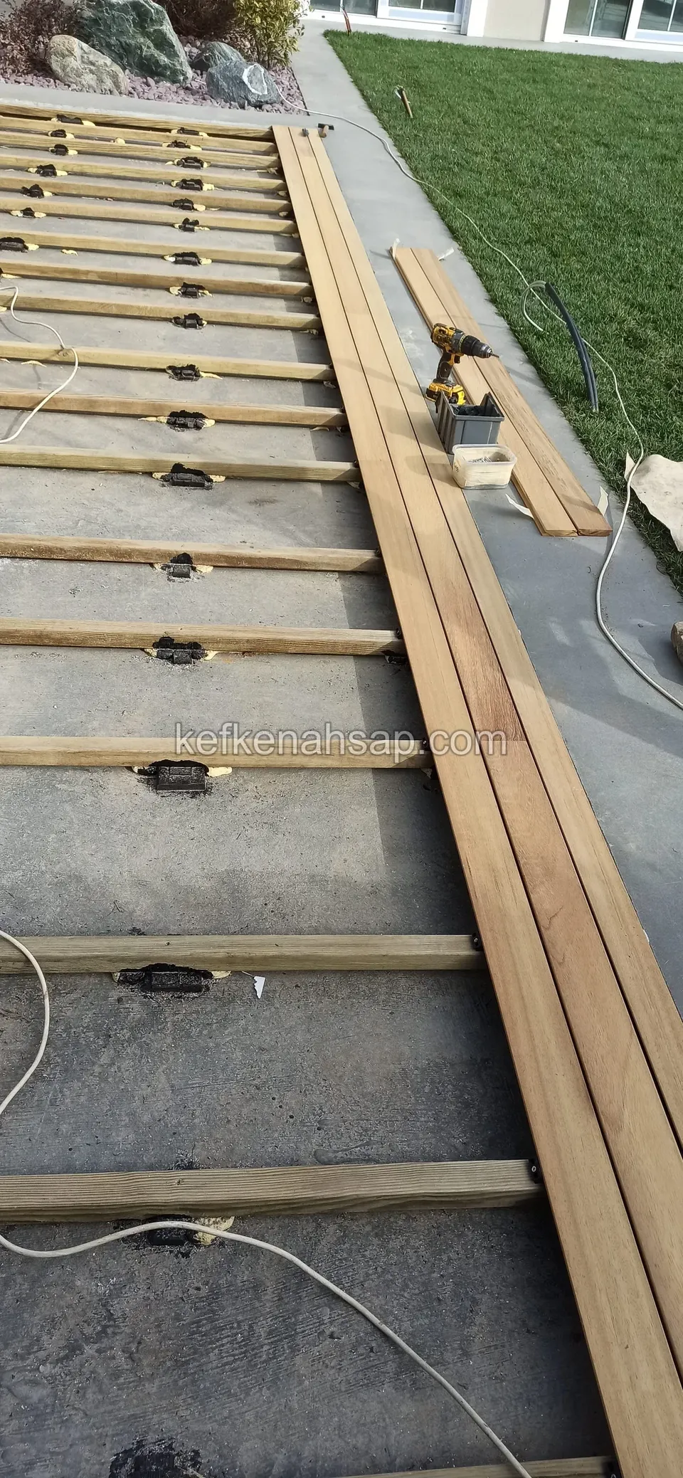 First deck boards placed side by side on pedestal-mounted joists, with a stack and an extension cable beside them