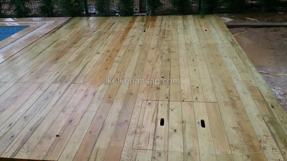 Damp, pale pine deck surface with a cover panel in the middle that has two long slots cut in it