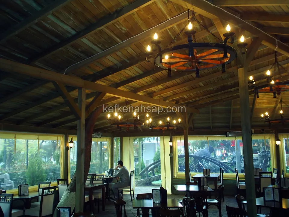 Camlı bölmelerle çevrili kafe salonunda kirişli ahşap tavan ve tekerlek biçimli avize