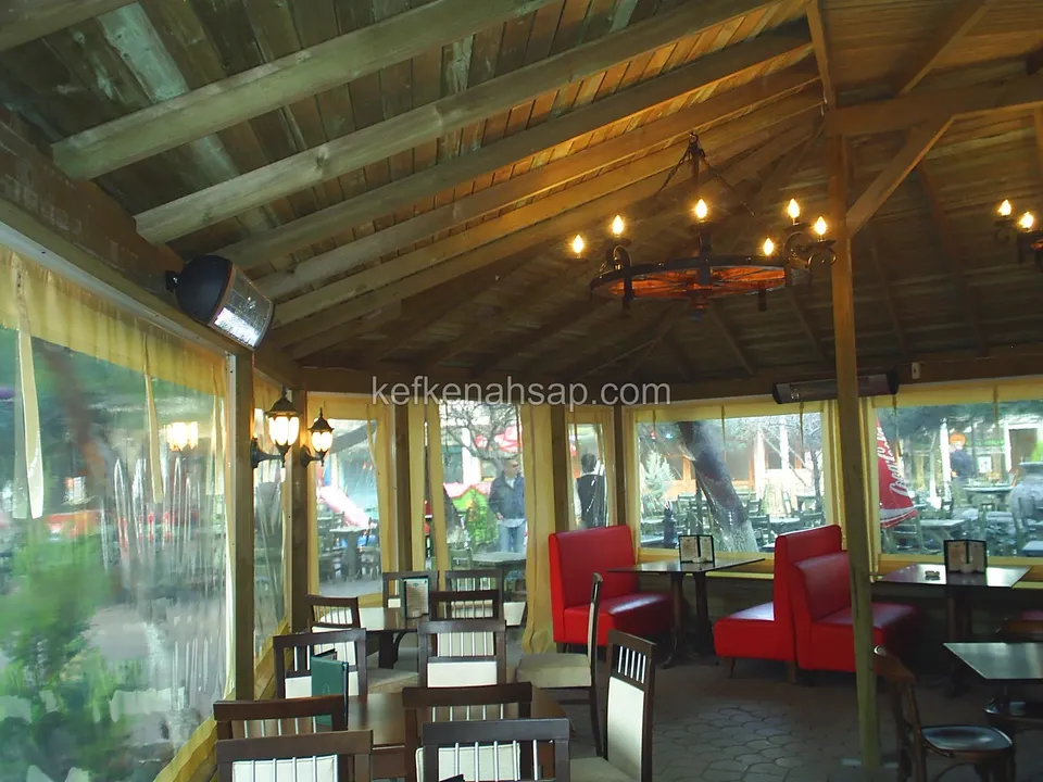 Ahşap kirişli çatının altında, kırmızı koltukların ve masaların dizildiği camlı kafe salonu
