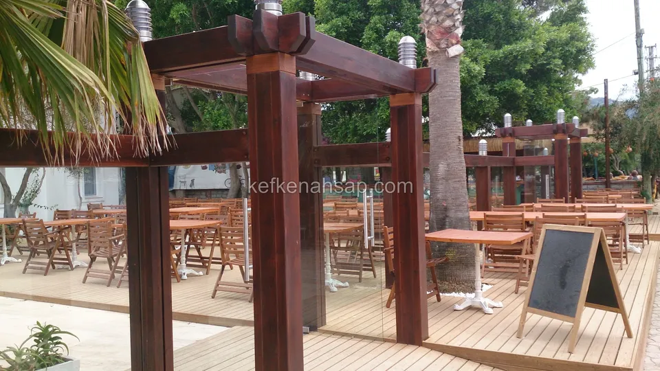Kafe terasında kalın direkli vernikli ahşap pergola, ahşap deck, masalar, sandalyeler ve menü tahtası