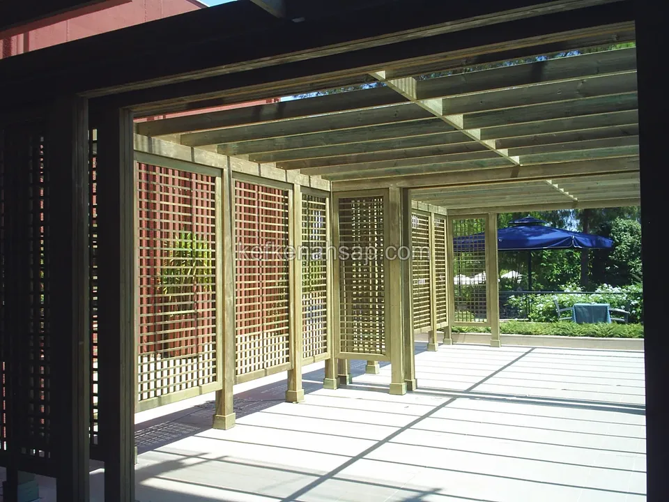Açık renk zeminli terasta, ahşap kafes panellerle bölünmüş, düz kirişli pergola altı