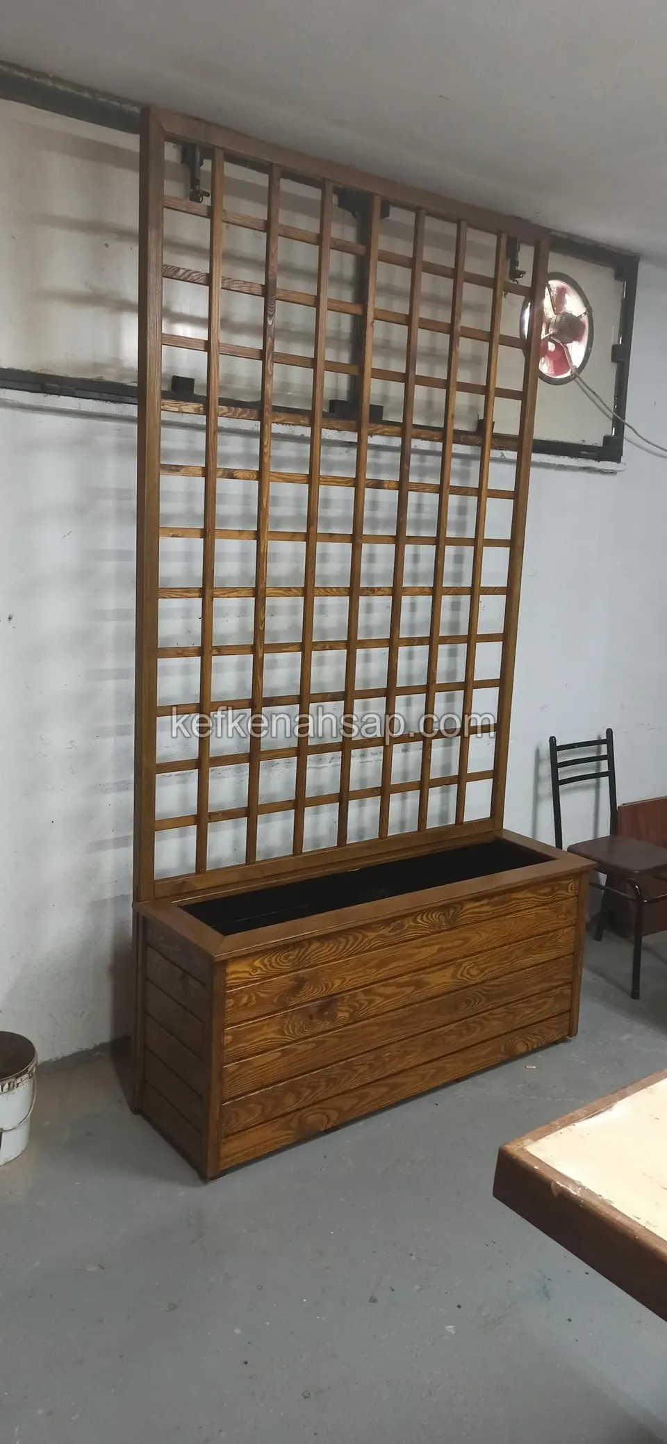 Duvar önünde duran, arkasında kare gözlü yüksek ahşap kafesi olan ceviz tonunda dikdörtgen çiçeklik