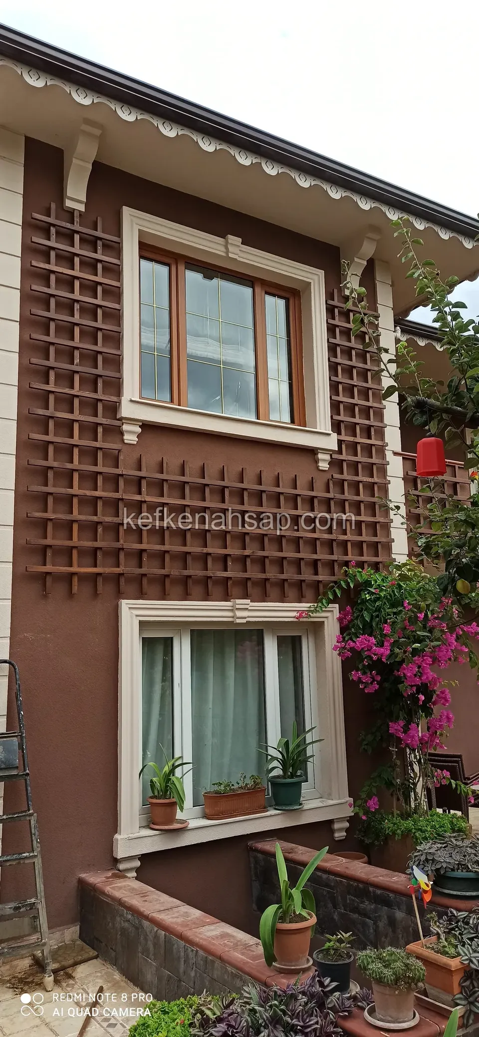 Square-mesh timber lattice panel covering the wall between and around two windows on a brown-painted house facade