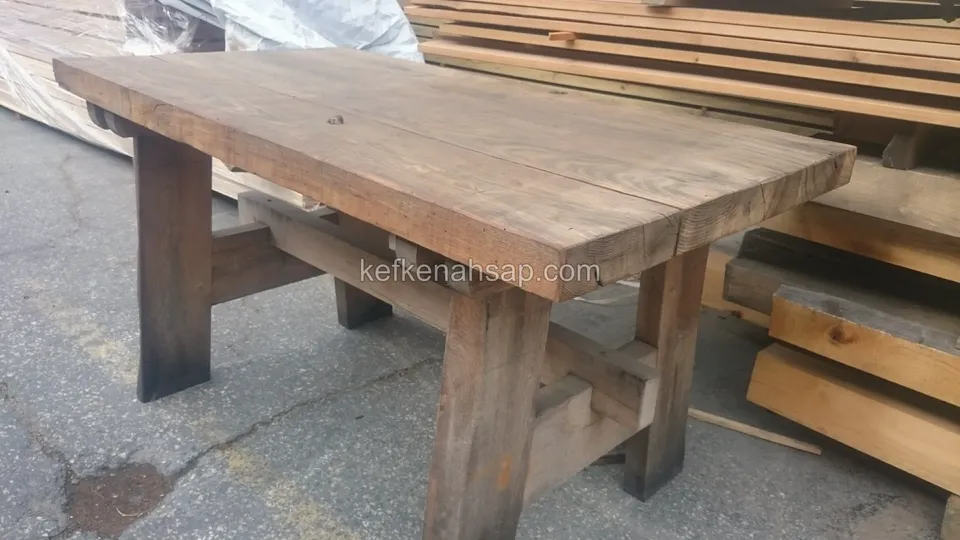 Ein langer massiver Holztisch aus dicken Bohlen, daneben gestapeltes Schnittholz