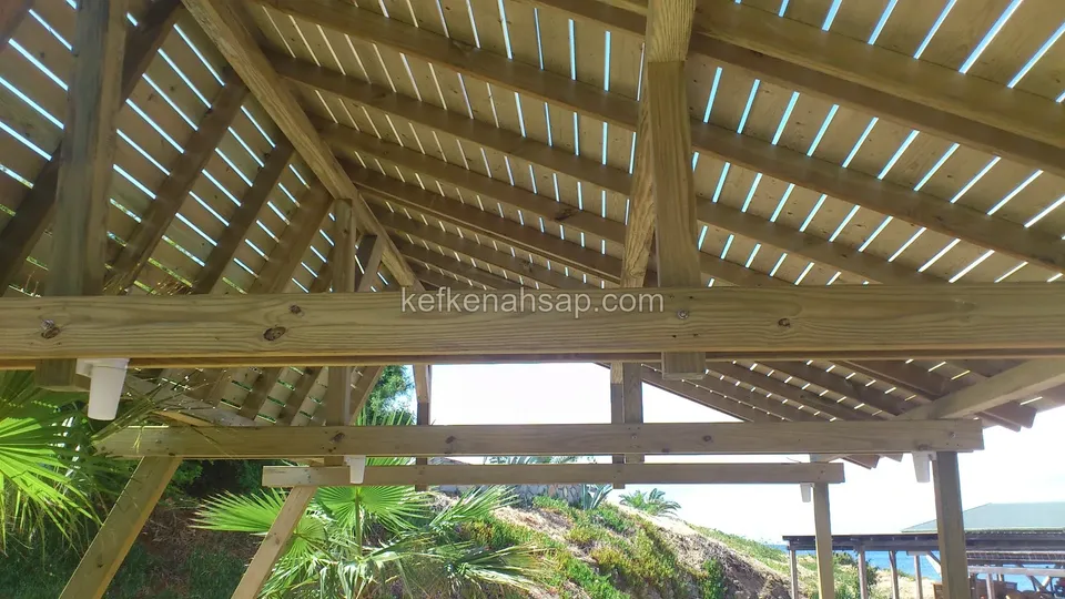 Gazebo roof rafters and closely spaced slats seen from below, with palms and the shore behind