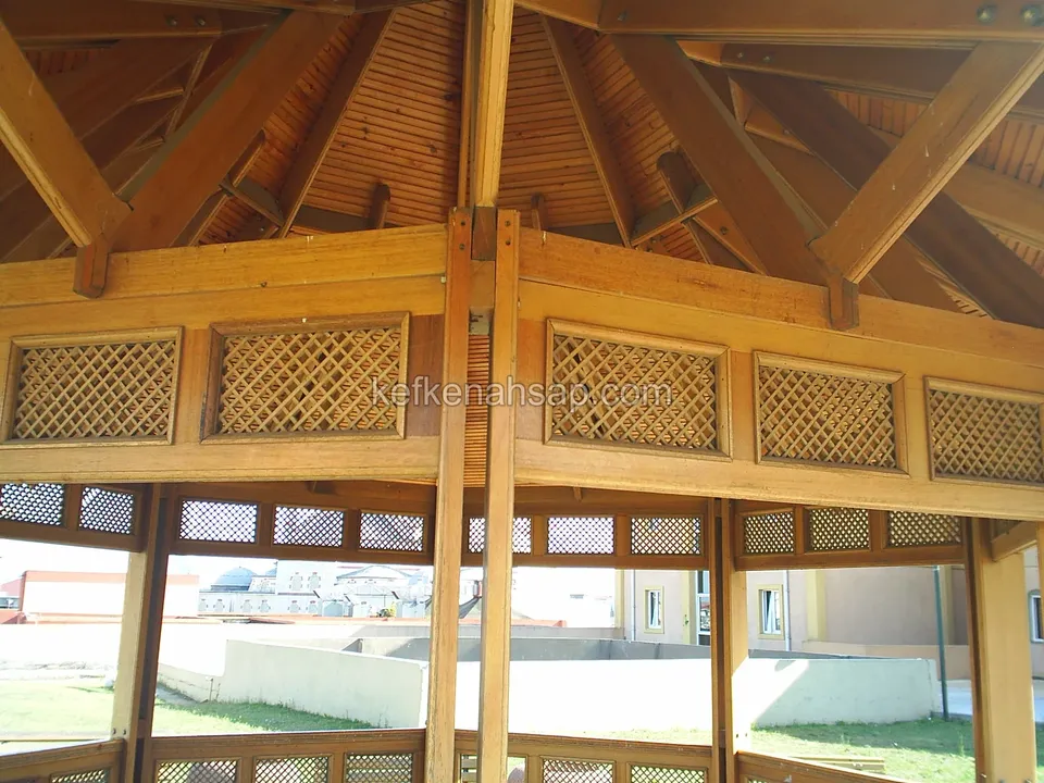 Inside a gazebo: roof beams, lining-board ceiling and a band of lattice panels, with a lawn and buildings behind