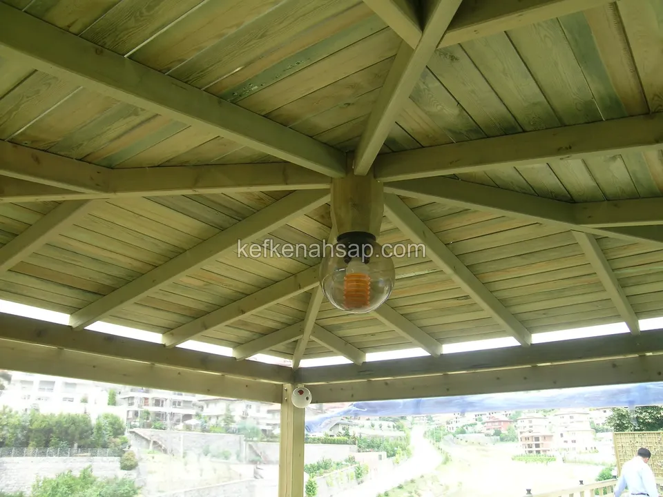 View from the centre of a gazebo ceiling: a bulb at the middle, beams fanning outward and lining boards, with a town behind