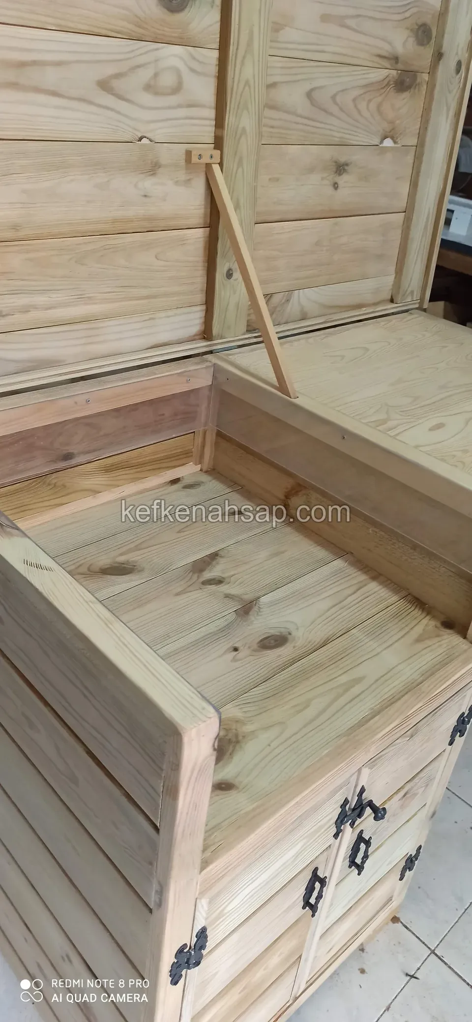 Eine Holztruhe mit offenem Deckel auf einem zweitürigen Schrank mit schwarzen Griffen und Scharnieren