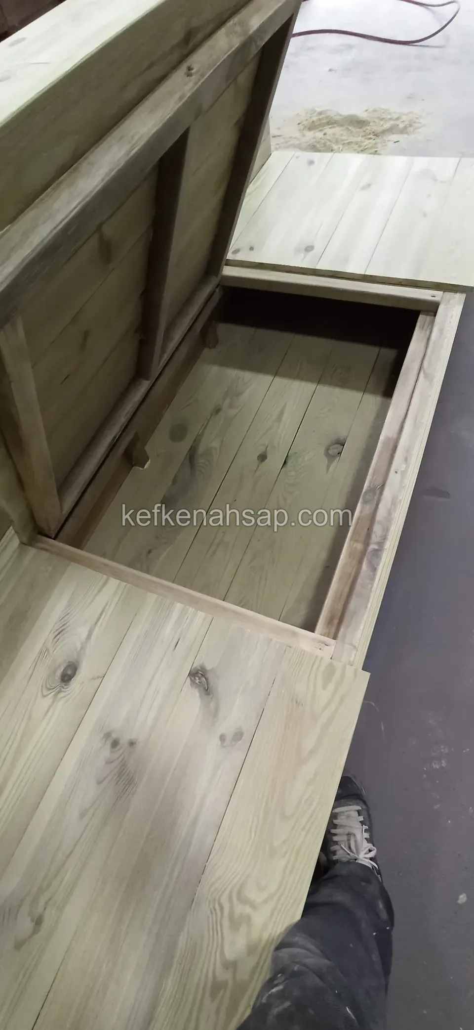 Das Staufach einer Holzbank, deren Sitz sich wie ein Deckel öffnet, aus Kiefernbrettern gebaut